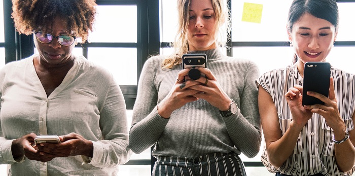 three women stand side by side on their phones