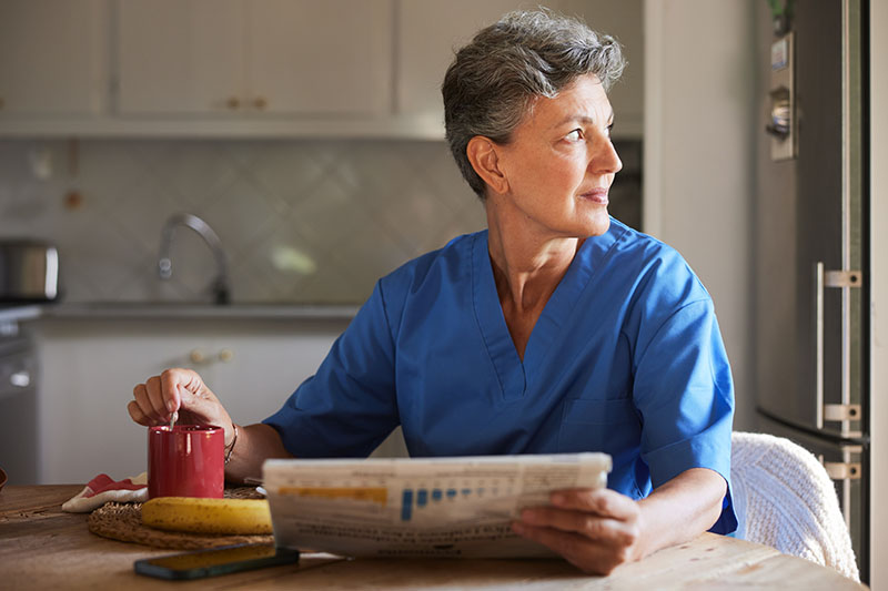 57-year-old in blue scrubs reading the newspaper at the breakfast table